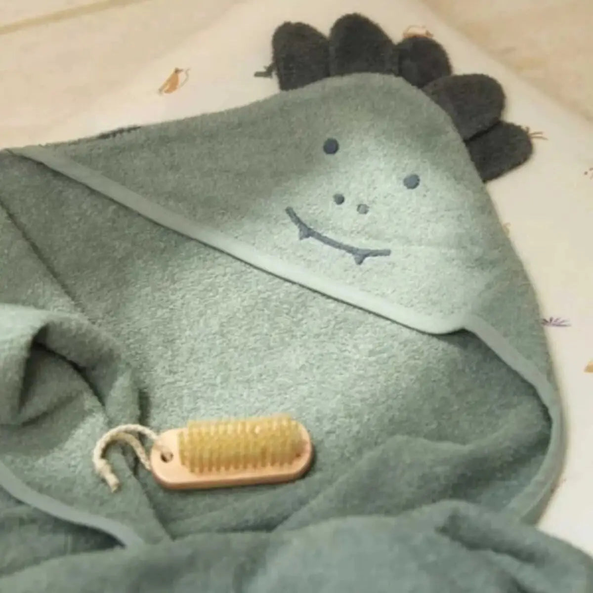 Green hooded towel with a face design and gold tag on a beige surface