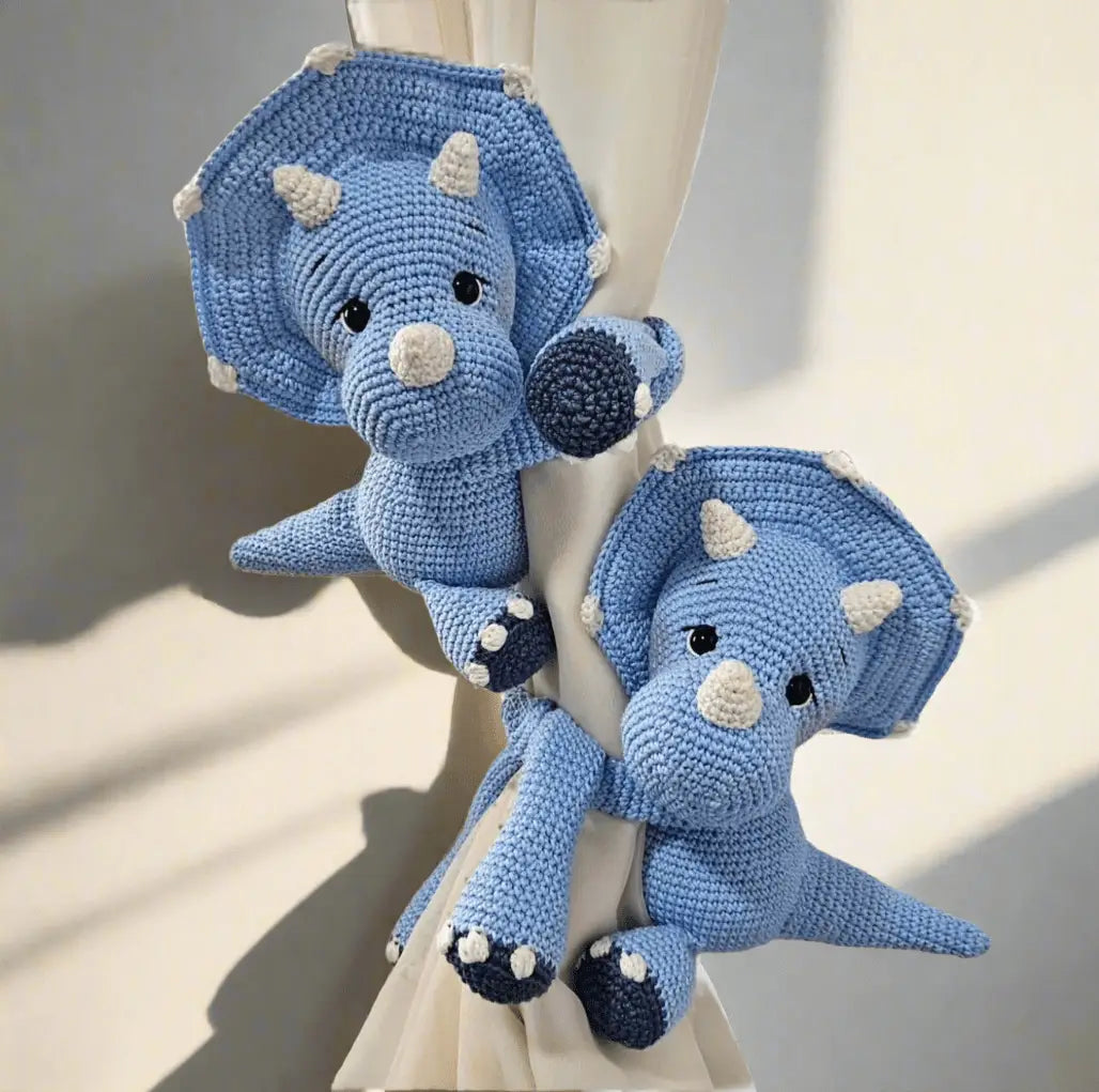 Blue crocheted triceratops dinosaur toys hanging on curtain with soft shadows