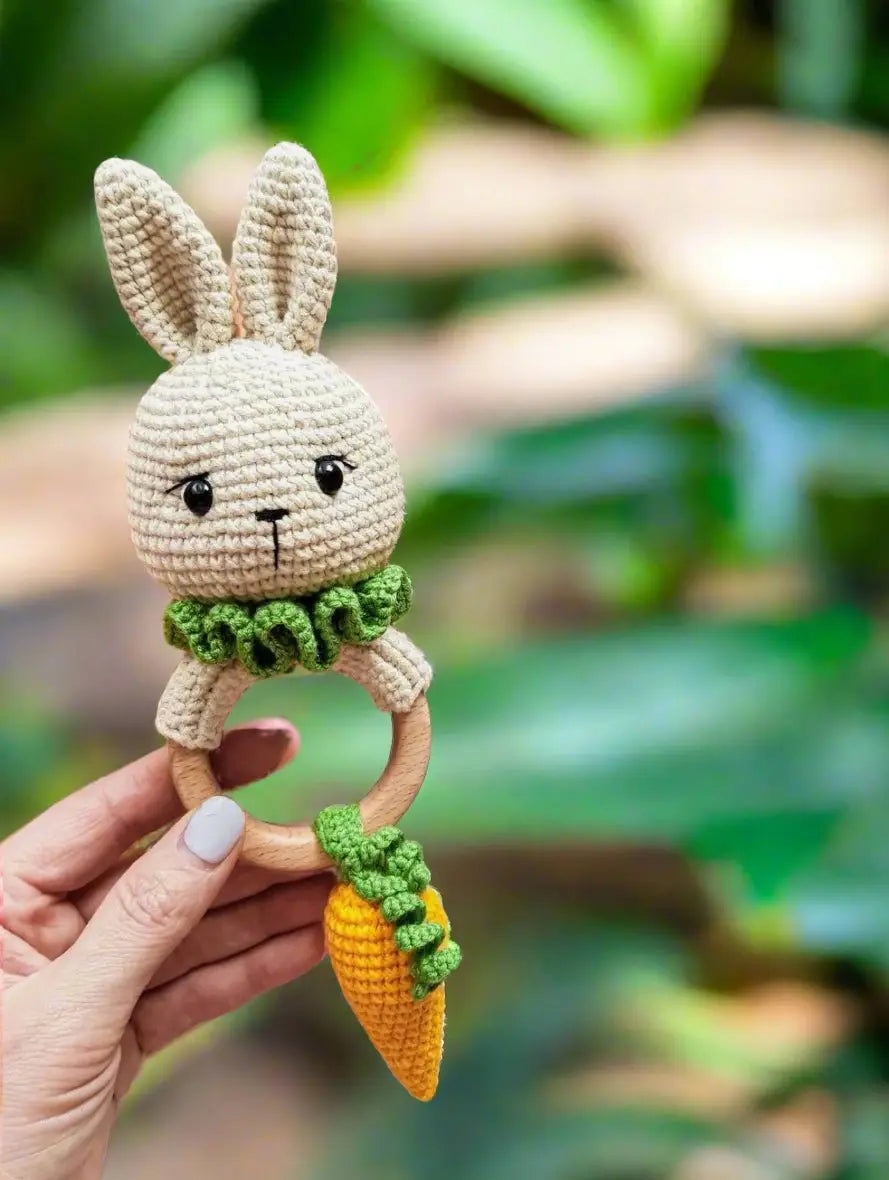 Crocheted bunny rattle with wooden ring and carrot-shaped toy, held by hand