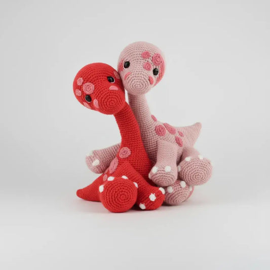 Two crocheted dinosaurs in red and pink, with polka dot details and curved necks.