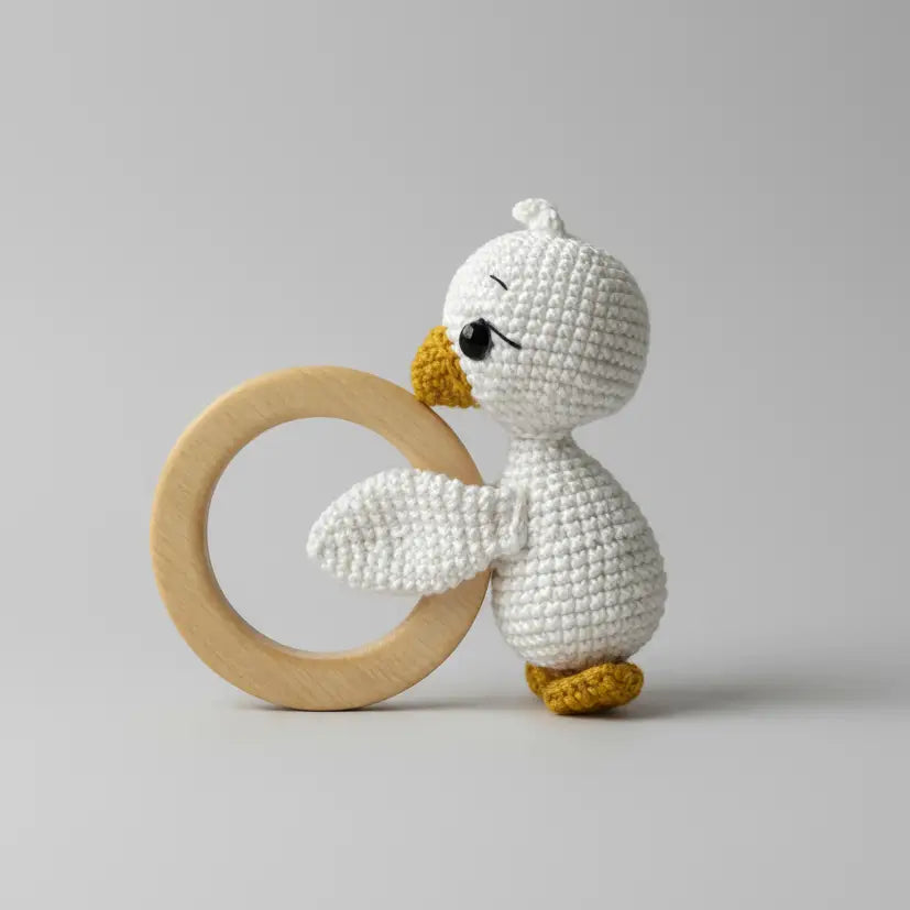 Crocheted white duck toy with yellow beak and feet, holding wooden ring