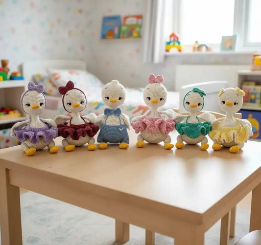 Six crocheted penguin dolls in colorful tutus sitting together on a wooden table in a playroom