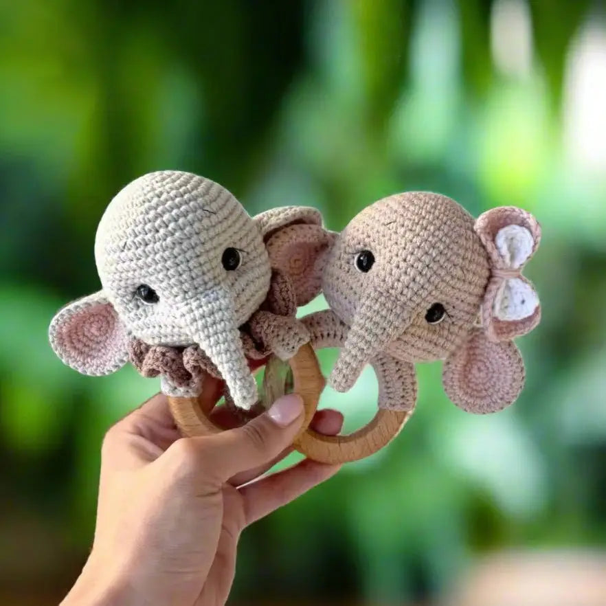 Crocheted elephant baby rattles on wooden rings, held by a hand outdoors