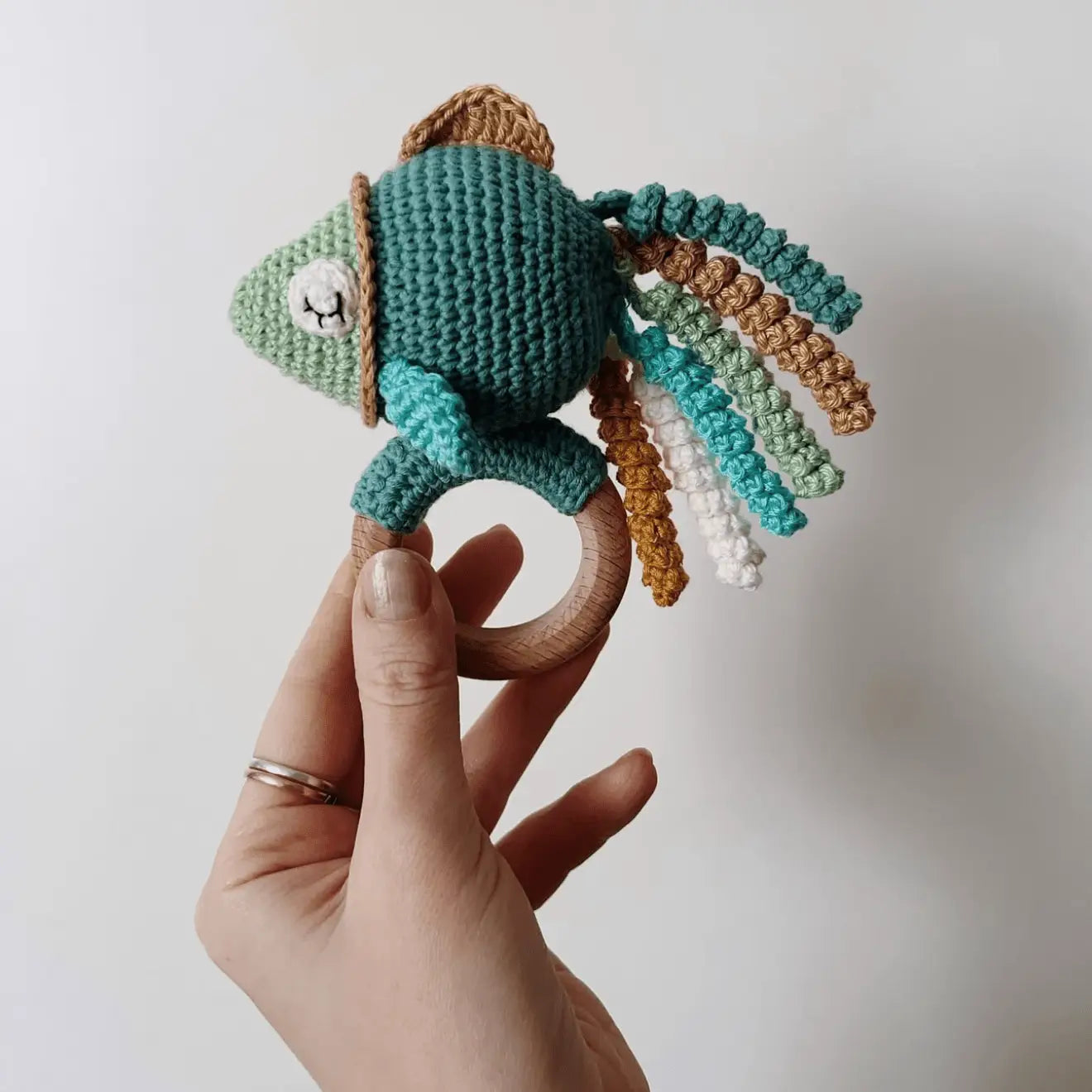 Crocheted chameleon teething ring with colorful curled yarn strands on wooden ring