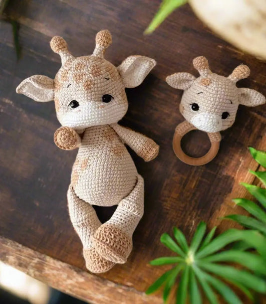 Crocheted giraffe toy and matching baby teething ring on wooden surface with plants