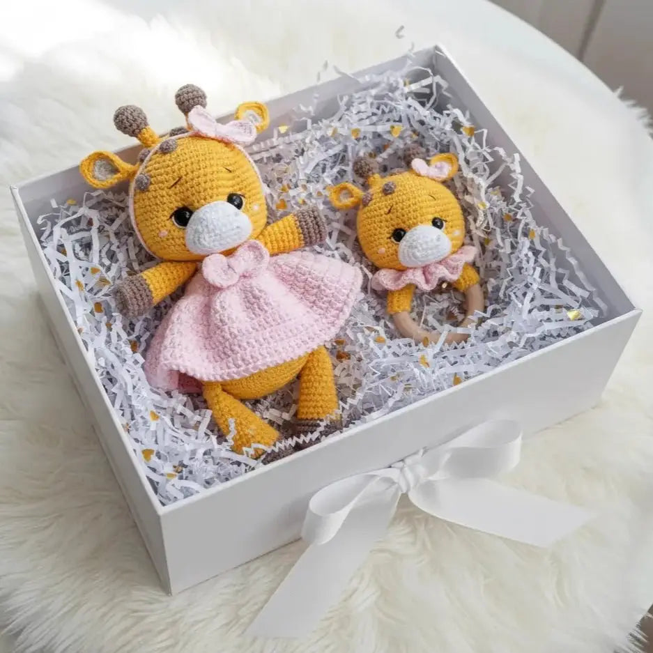 Two crocheted yellow giraffe dolls in a gift box with white shredded paper and a bow