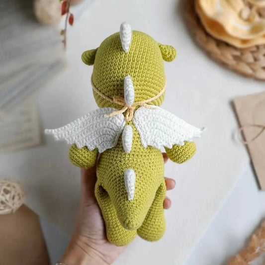 Green crocheted dragon with white wings, held in a hand with a bracelet.
