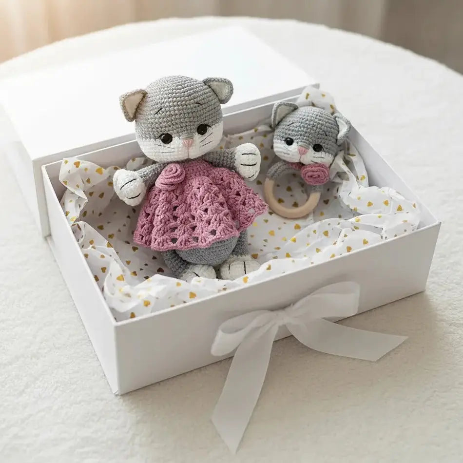 Two crocheted gray cats with pink sweater and wooden teething ring in a gift box with gold hearts
