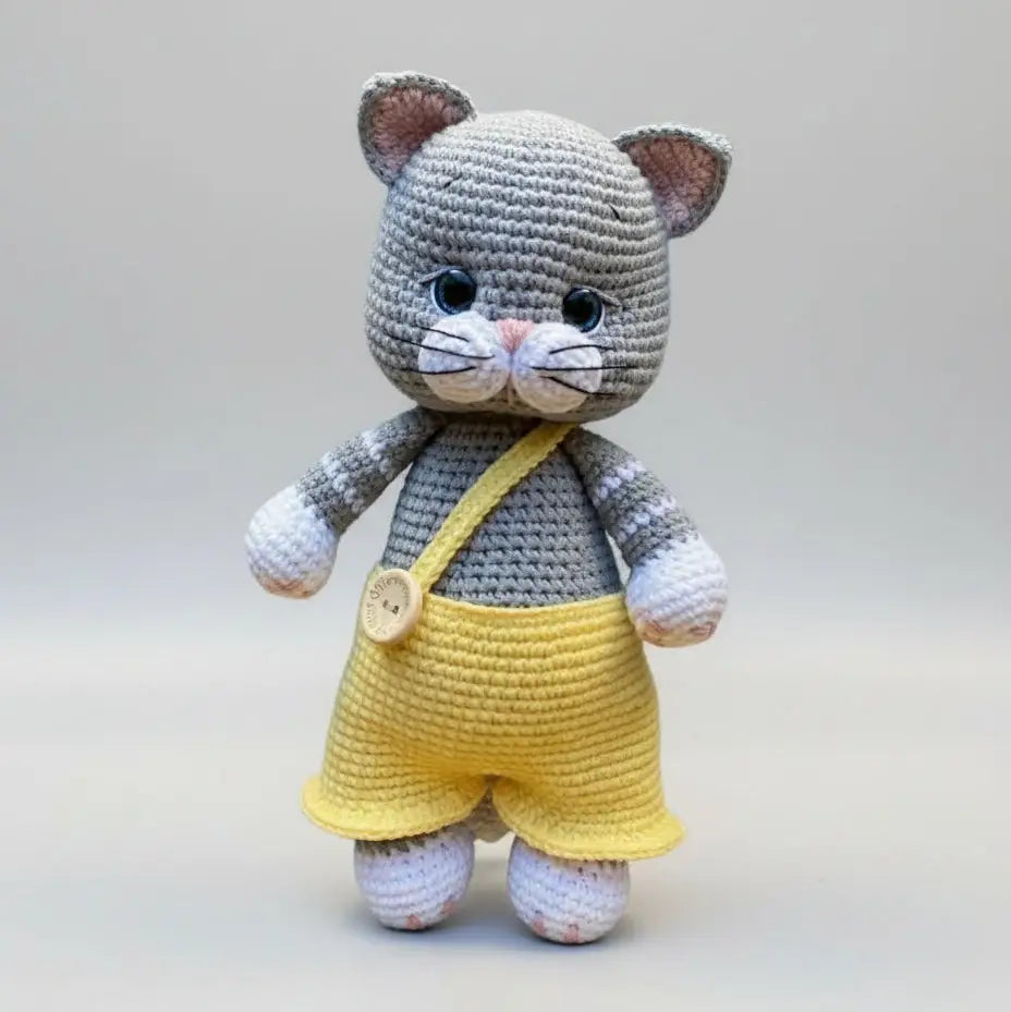 Crocheted gray cat in yellow overalls with a cute button and shoulder bag