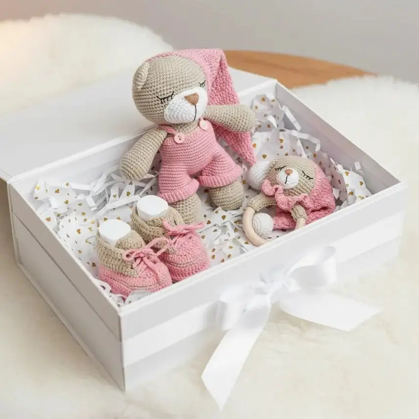 Pink and beige knitted baby toys in a gift box with white ribbon and gold dots