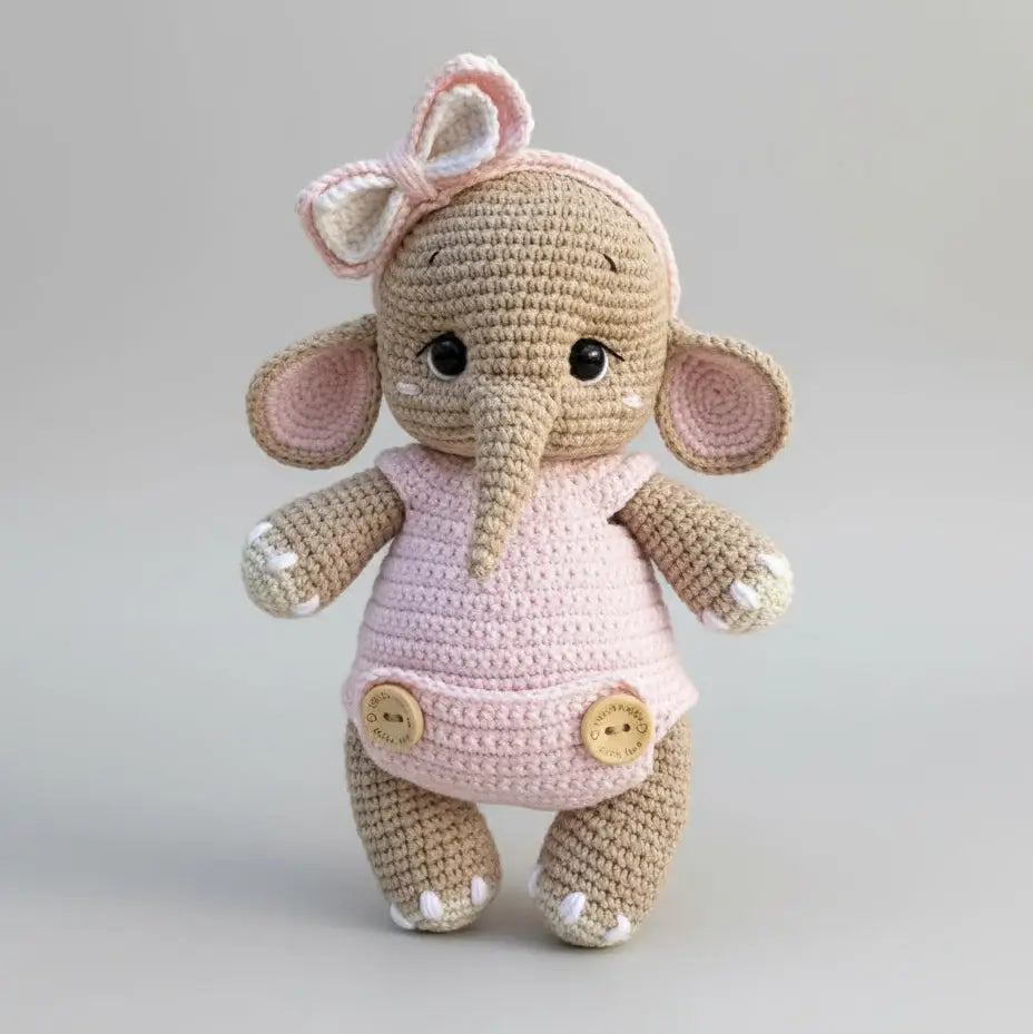 Crocheted elephant stuffed animal wearing pink dress with bow and buttons
