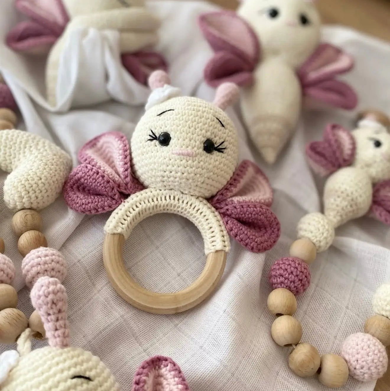 Crocheted baby rattle and toys in white, pink, and wood tones, with bunny-like characters
