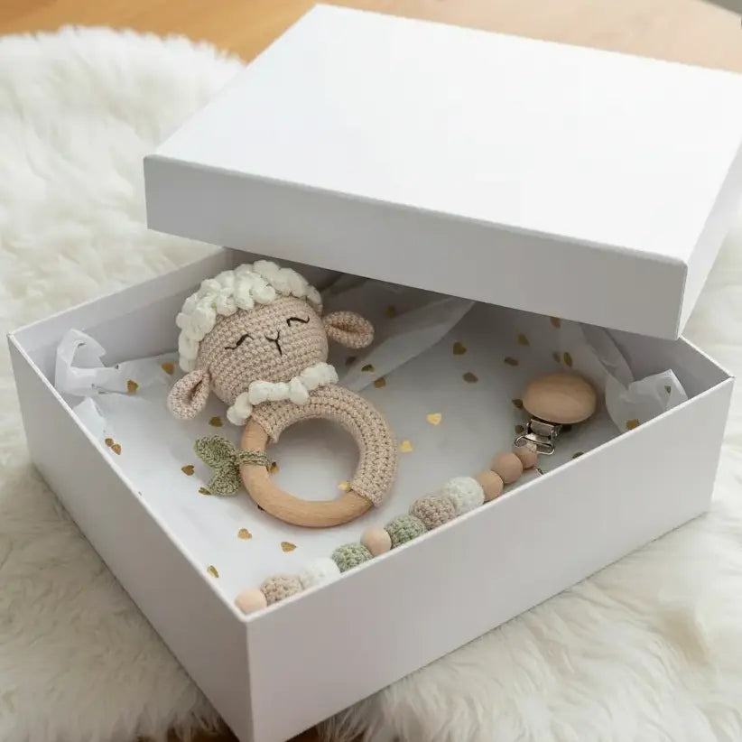 Crocheted sheep rattle and wooden beads in a white box on a fluffy white surface.