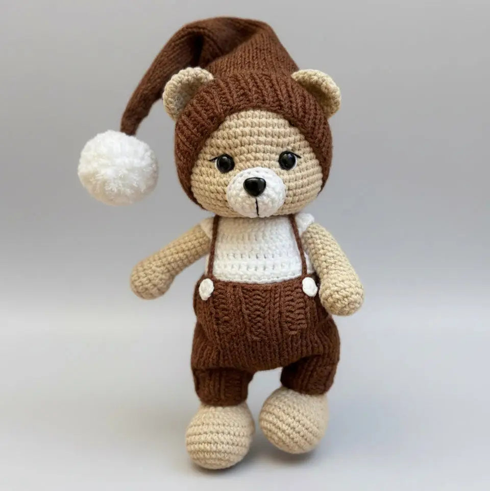 Crocheted teddy bear in brown overalls and nightcap with white pompom