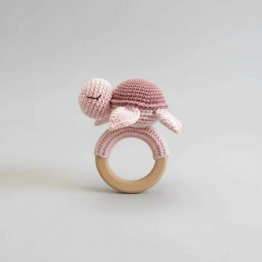 Crocheted turtle rattle with wooden ring on a light gray background
