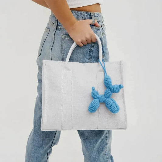 White tote bag with blue crocheted charm hanging, held against denim jeans