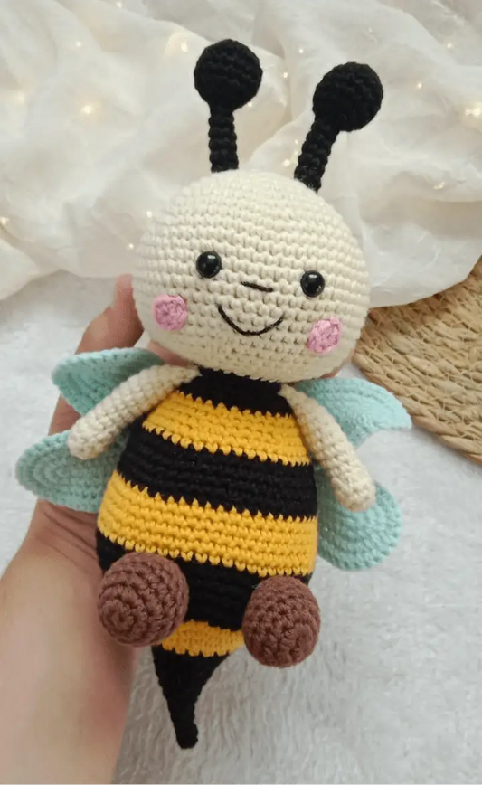 Crocheted bee plushie with cute face, black and yellow stripes, teal wings