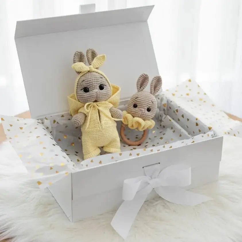 Two crocheted bunny dolls in yellow and gray, nestled in a gift box with gold polka dots.