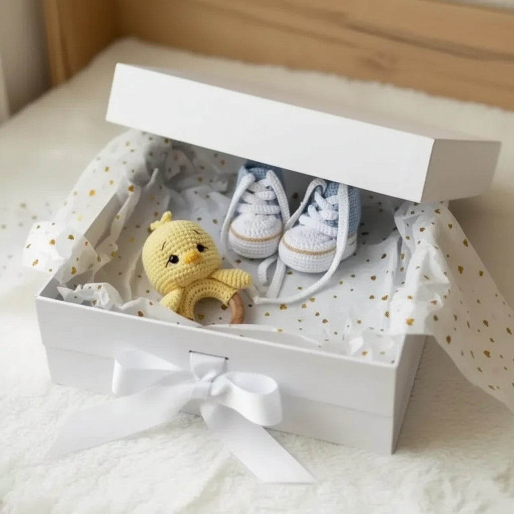 Crocheted yellow chick and blue baby booties nestled in a gift box with white ribbon