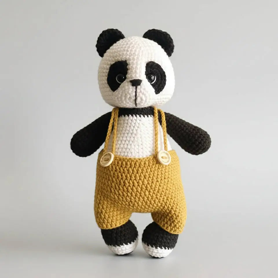 Crocheted panda bear wearing yellow overalls, standing against a neutral background