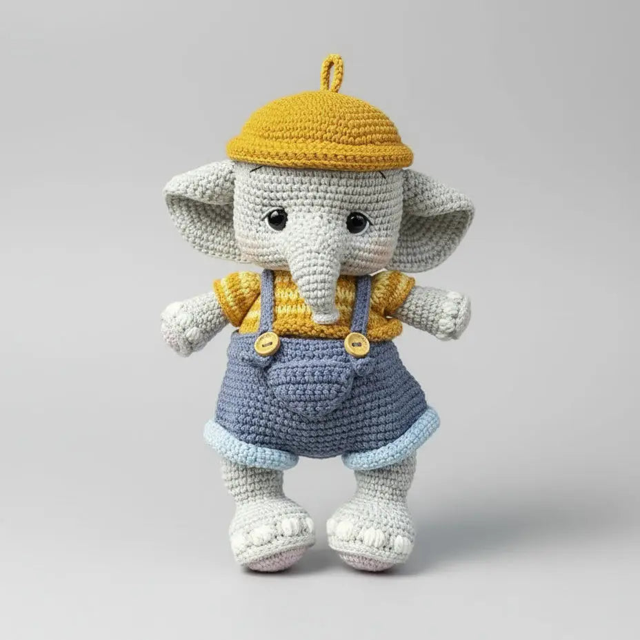 Crocheted elephant doll wearing yellow hat and blue overalls on gray background