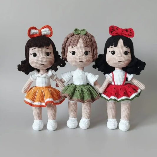 Three crocheted dolls with curly hair and bows, wearing colorful skirts and white tops