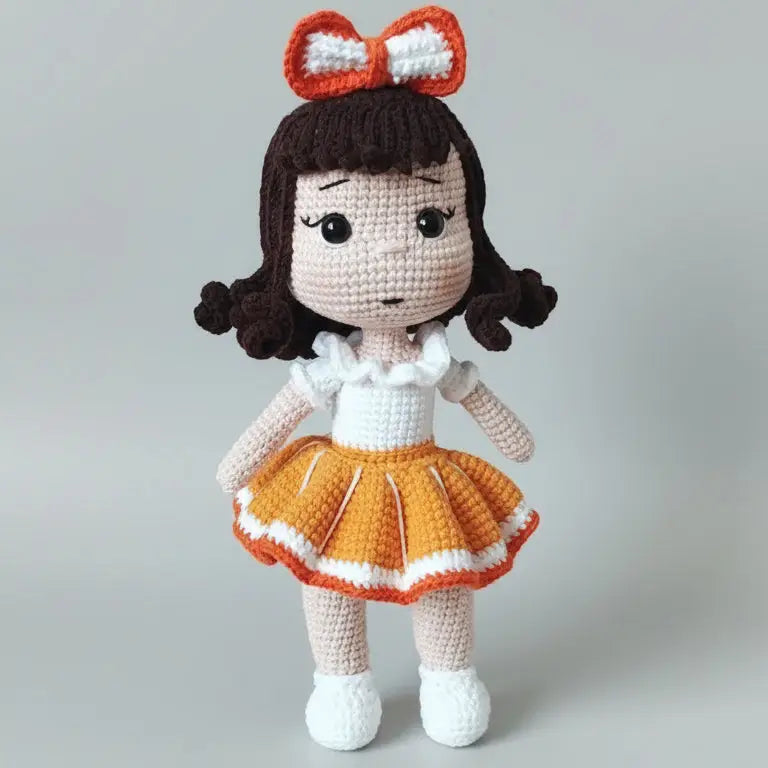 Crocheted doll with curly hair, orange bow, and yellow-orange pleated skirt