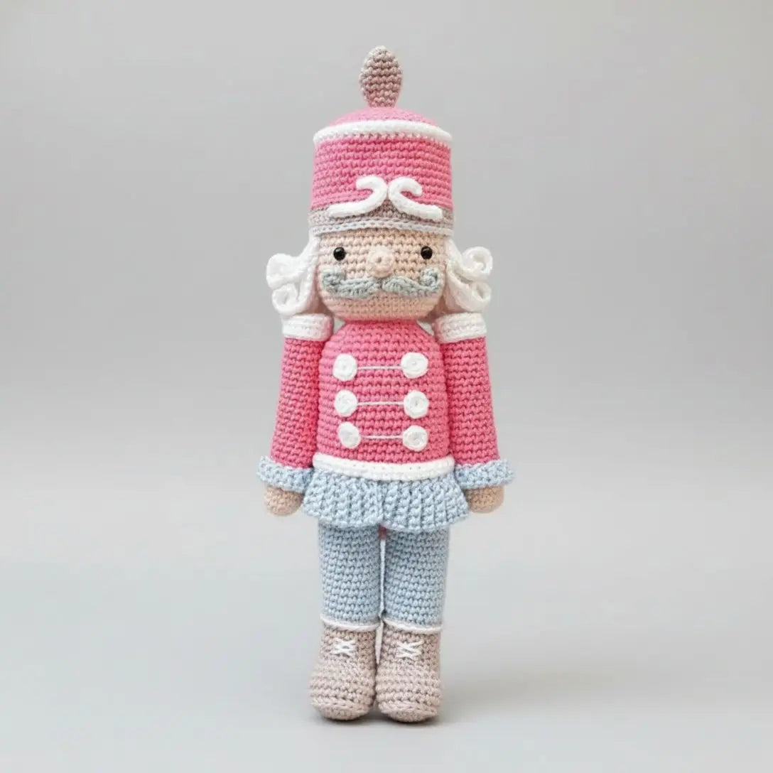 Crocheted nutcracker doll in pink and blue with curly hair and mustache, standing upright