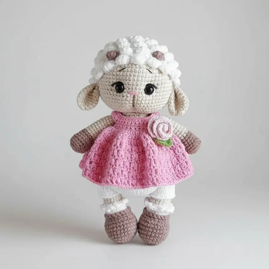 Crocheted lamb stuffed animal wearing pink dress with flower and white socks