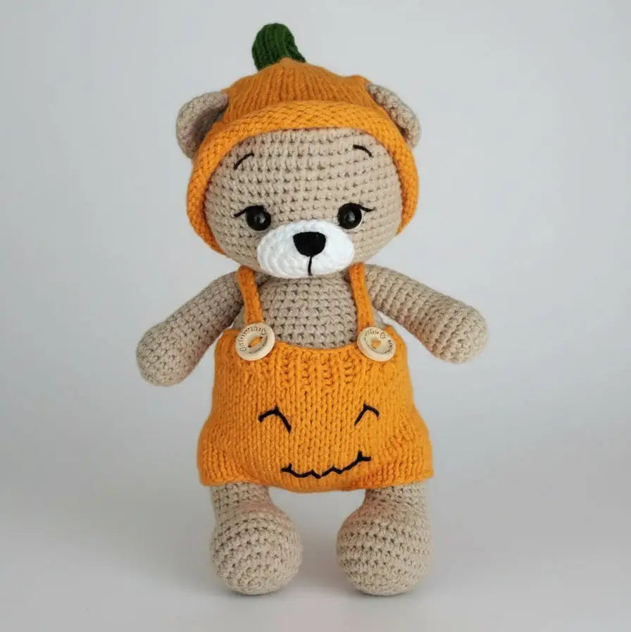 Crocheted teddy bear in orange pumpkin costume with cute smile on white background