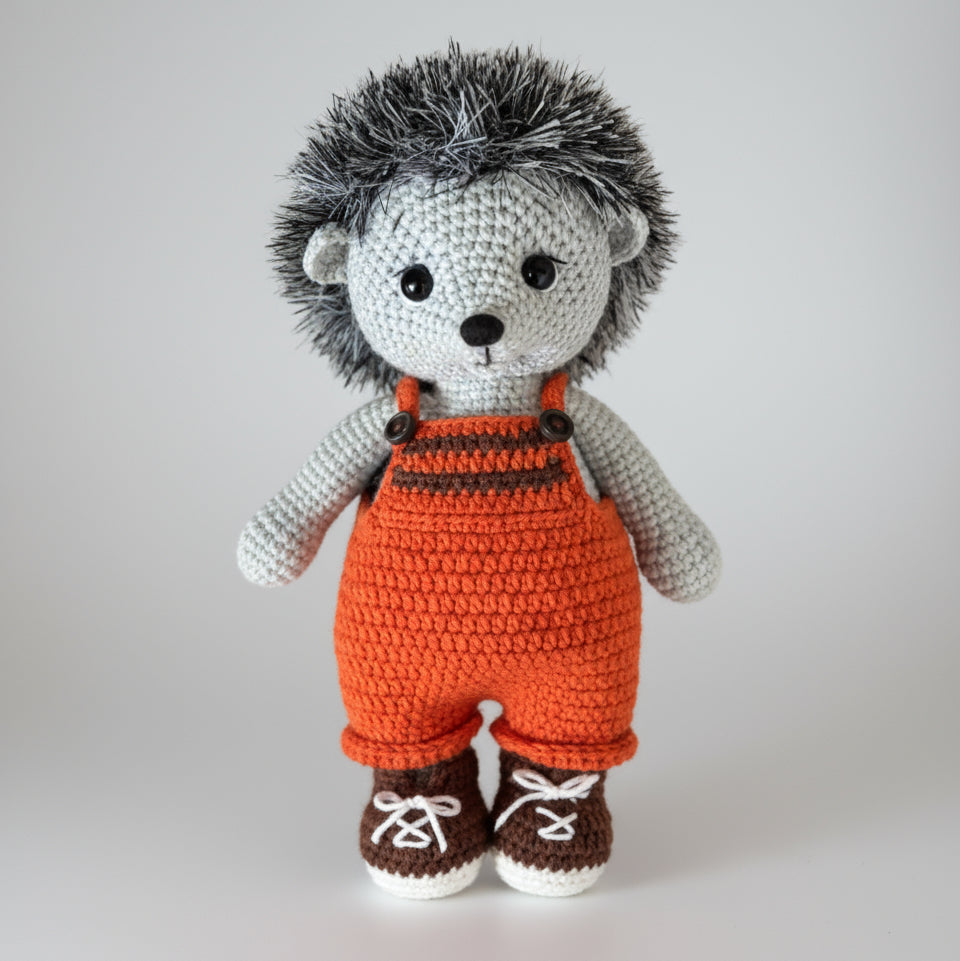 Crocheted hedgehog wearing orange overalls and brown sneakers on a white background