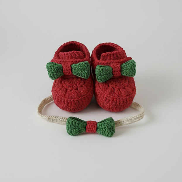 Red crochet baby booties with green bow and matching headband on white background