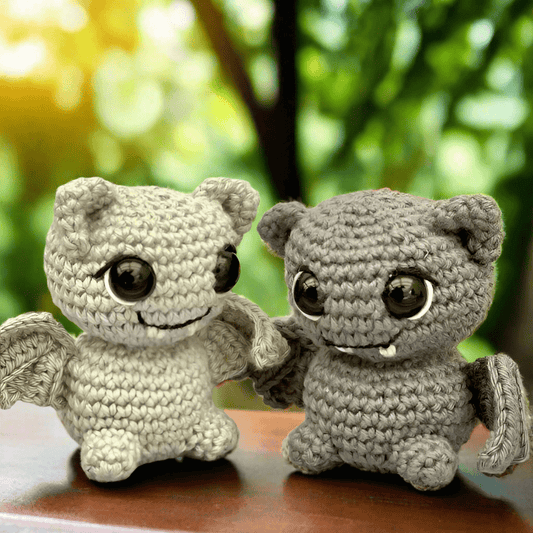 Two crochet creatures with big eyes sitting together, smiling on a blurry green background
