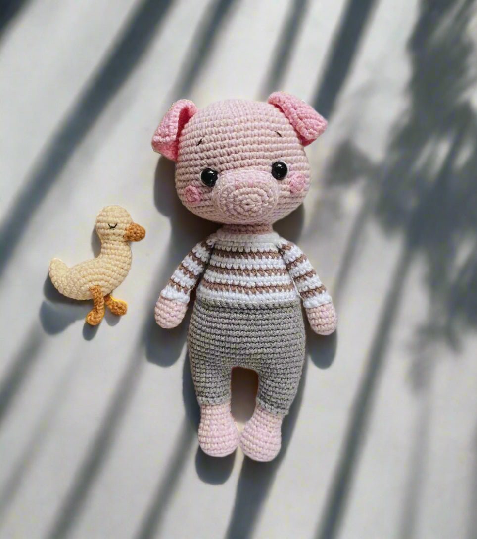 Crocheted pink pig in striped sweater with small yellow duck companion