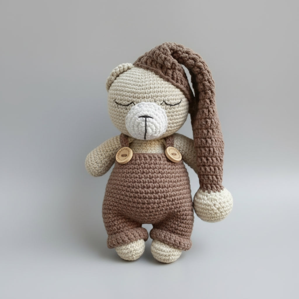 Crocheted teddy bear in brown and cream, wearing overalls with wooden buttons