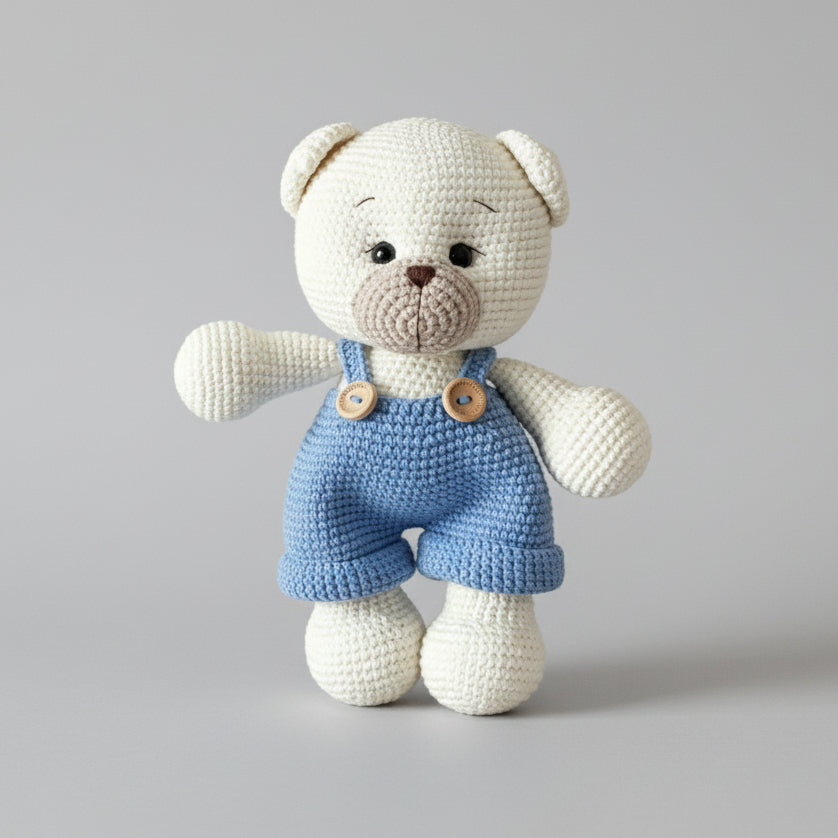 Crocheted white teddy bear wearing blue overalls with wooden buttons