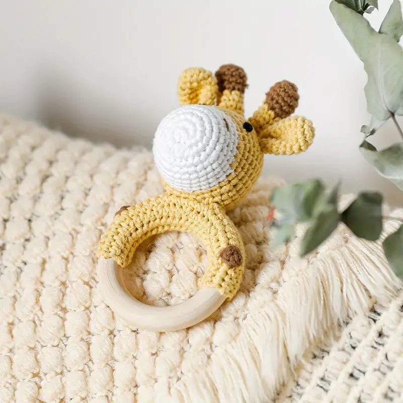 Crocheted yellow giraffe baby teething ring on textured cream blanket
