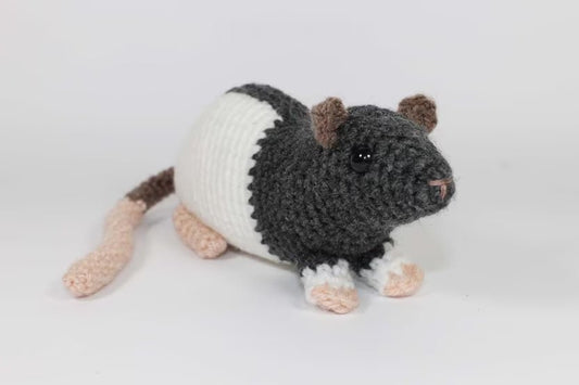 Crocheted rat plushie with black and white body and pink limbs on white background