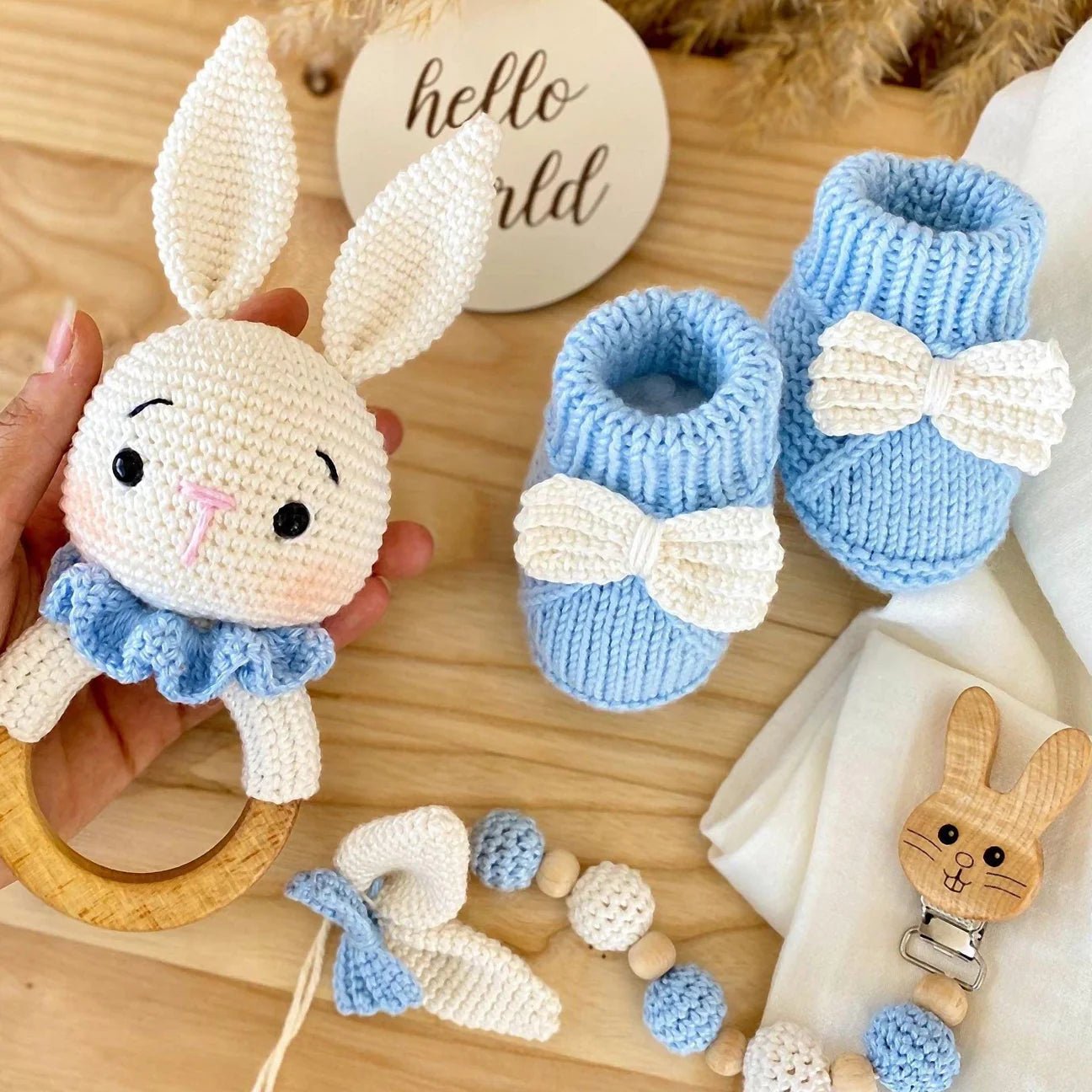 Crocheted white bunny, blue booties, wooden teething ring, and pacifier clip on wooden background