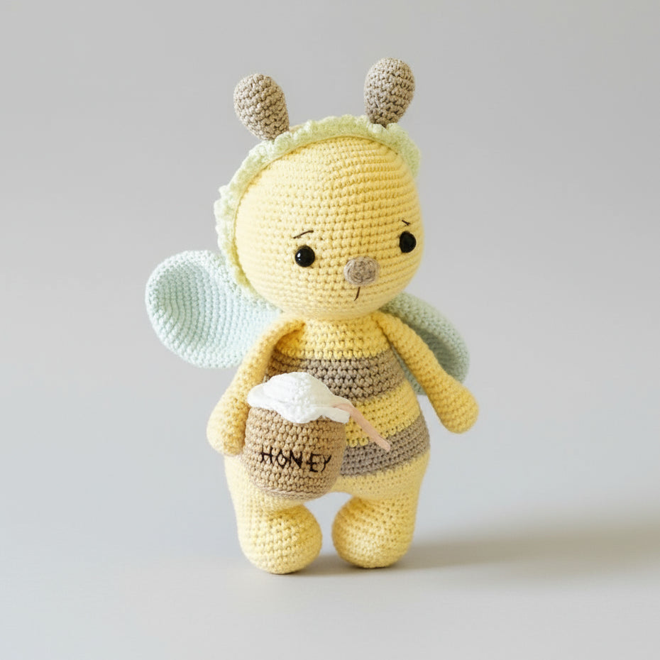 Crocheted yellow bee stuffed animal holding a tiny honey pot on grey background