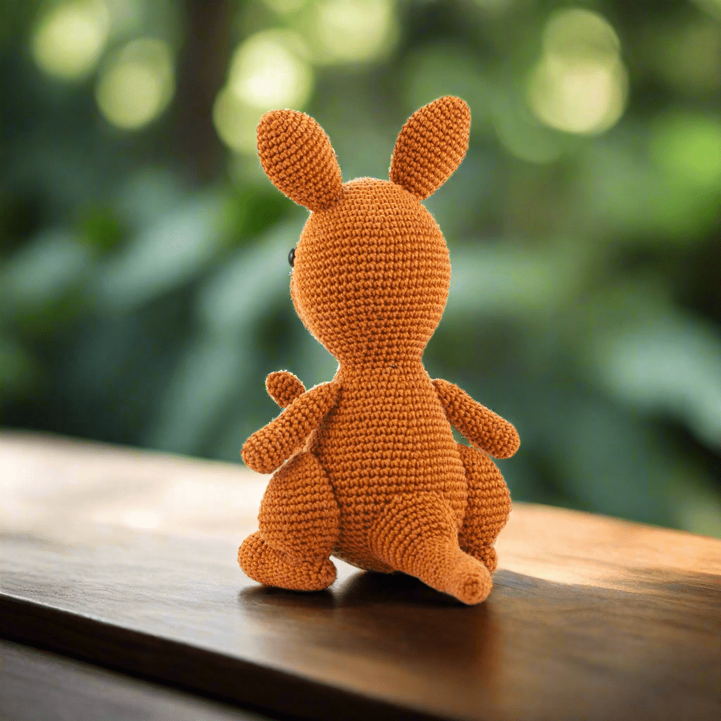 Orange crocheted bunny sitting on wooden surface with blurry green background