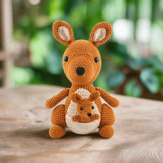 Crocheted orange kangaroo with baby joey in pouch, sitting on wooden surface