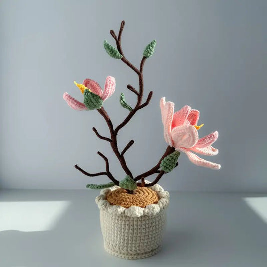 Crocheted pink flowers on brown branch in white textured pot against soft background