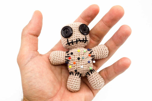 Crocheted voodoo doll with button eyes and colorful pins on an open palm