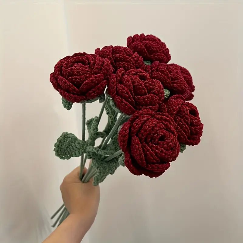 Crocheted deep red roses with green stems held in a hand against a white background