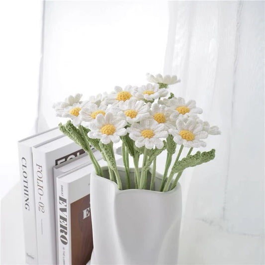 White crocheted daisies in a white vase, nestled beside minimalist books on a soft background.