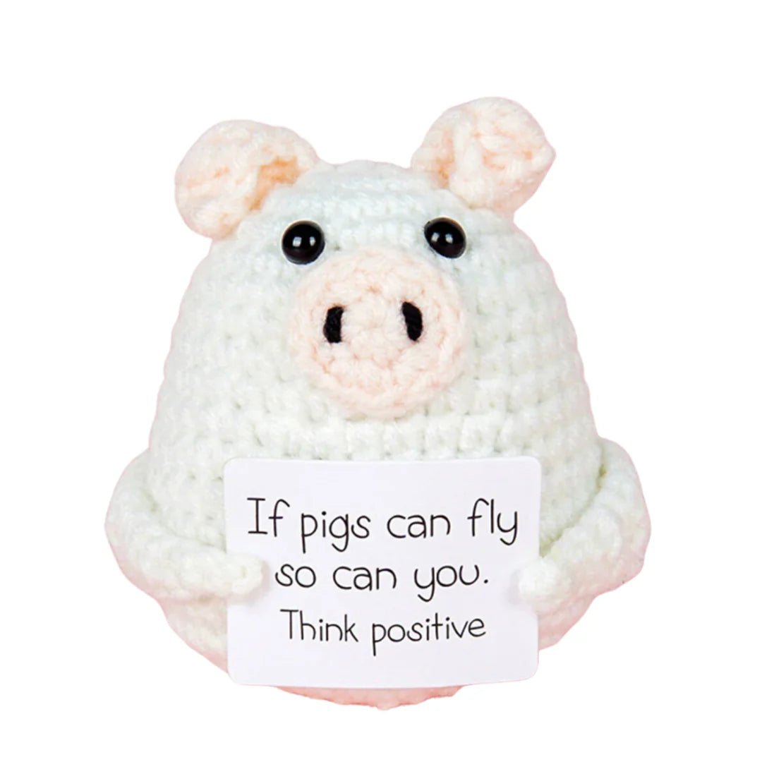 Crocheted white pig holding a motivational "Think positive" sign with playful message