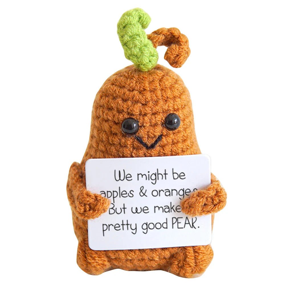Crocheted pear character holding a punny sign about apples, oranges, and pears