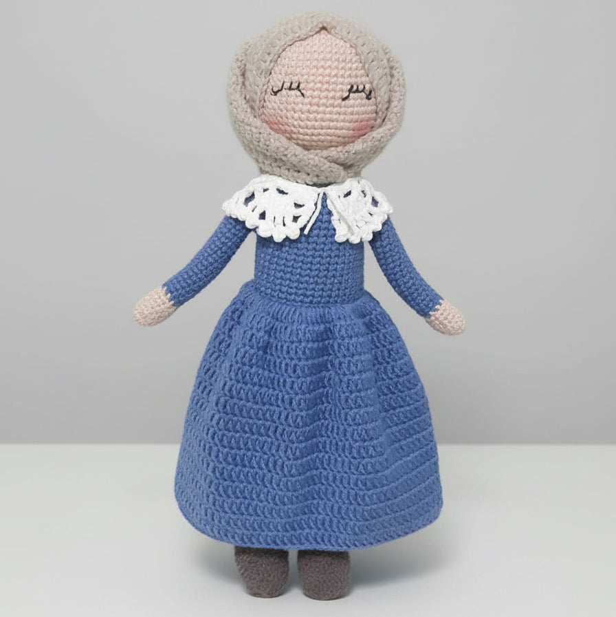 Crocheted doll in blue dress with white lace collar, serene expression, soft gray hair