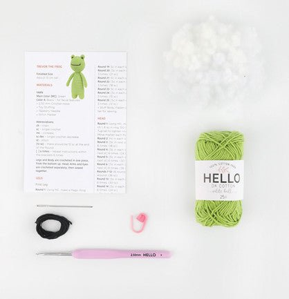 Green yarn, crochet hook, pattern, and small frog craft project materials laid out neatly